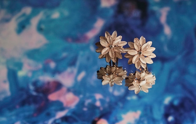 Pink flower shaped earrings on a mirror reflected with blue and pink background