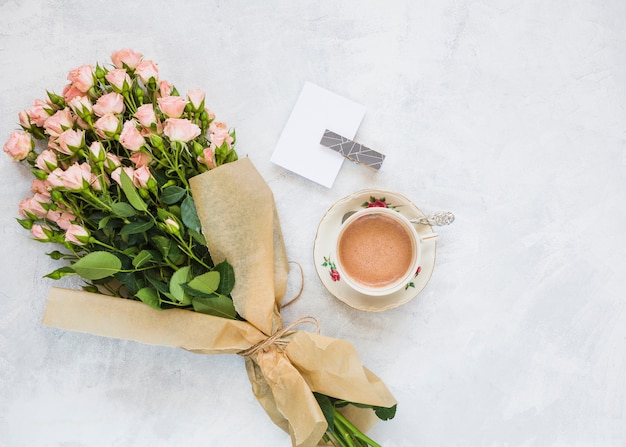 Bouquet di fiori rosa; carta e tazza di caffè su sfondo concreto