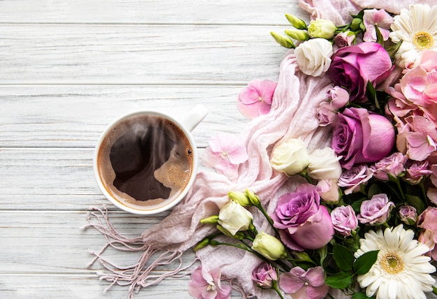 Pink flowers and cup of coffee on a white wooden background