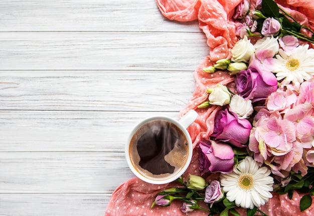 Pink flowers and cup of coffee on a white wooden background