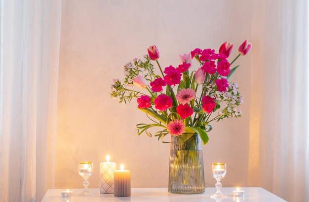 pink flowers in glass modern vase with burning candles in white interior