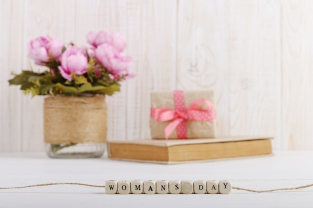 Розовые цветы в вазе, книга и подарок на столе