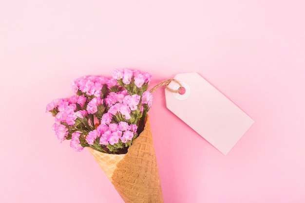 Pink flowers in a waffle ice cream cone on a bright background next to a blank label. 