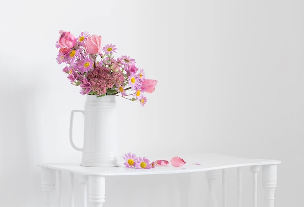 Pink flowers in white jug on background white wall