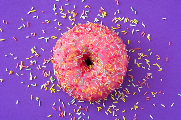 Pink frosted donut with colorful sprinkles isolated on purple