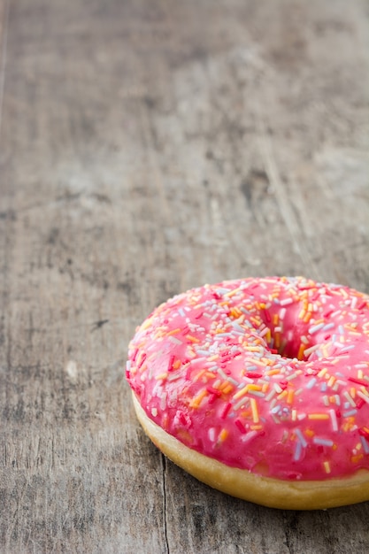 Pink frosted donut with colorful sprinkles on wooden table copy space