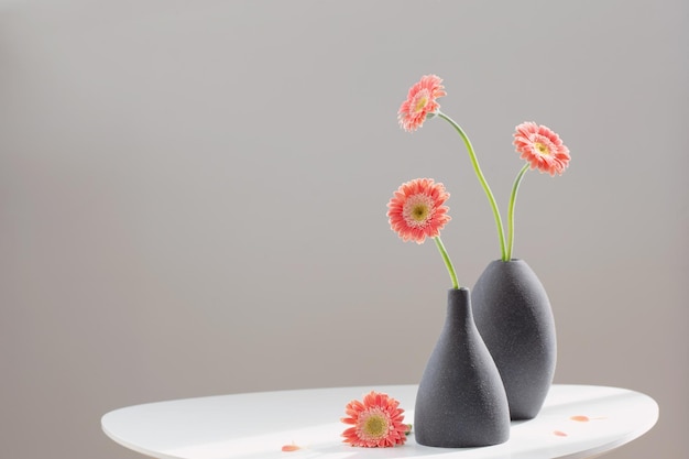 Pink gerber in gray vases on white table on background gray wall