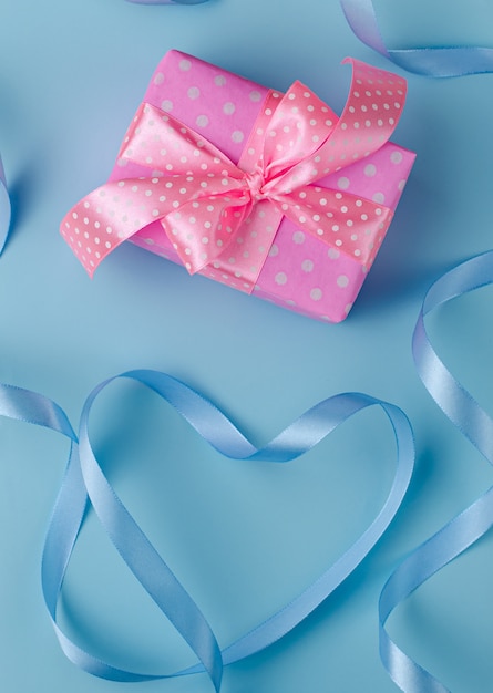 Розовая подарочная коробка или подарок с лентой на пастельно-синем фоне