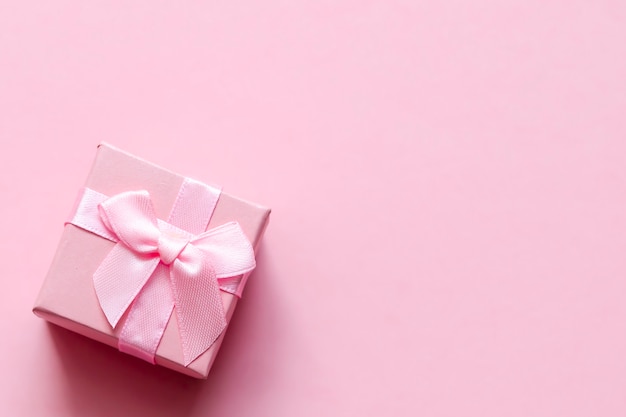 Pink gift box with bow on pink pastel background. Festive backdrop. Top view. Copy space.