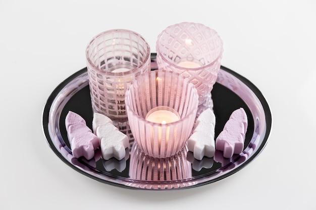 Pink glass candlesticks with candles and marshmallows on a metal plate White background