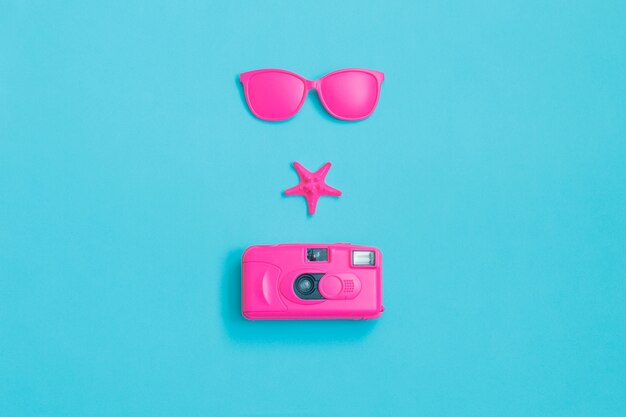 Pink glasses, camera and starfish on blue background