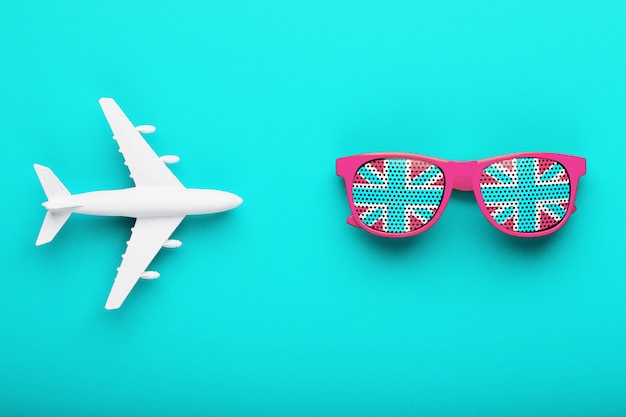 Pink glasses with the flag of the United Kingdom in lenses on a blue surface with a white airplane