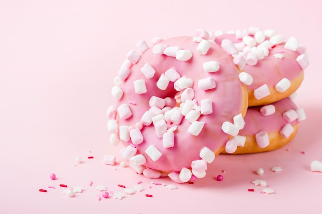 Pink glazed donuts with marshmallows on pink background close-up.