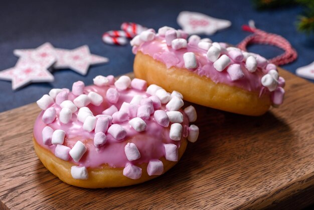 木製のカッティングボードにクリスマスの装飾が付いたピンクのグラスドーナツとマーシュマロウ