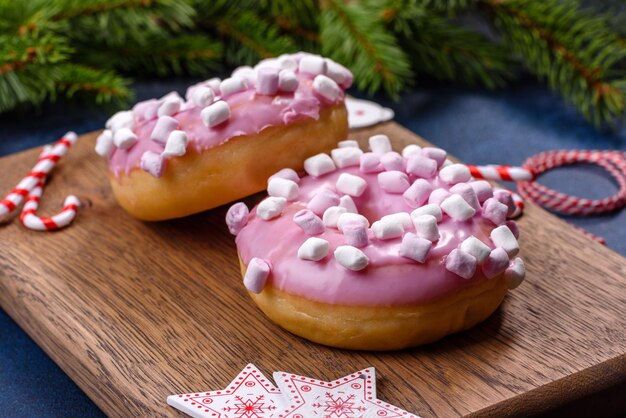 Pink glazed doughnut and marshmallow with Christmas decorations on a wooden cutting board