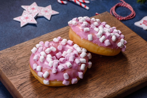 나무 커팅 보드에 크리스마스 장식이 있는 분홍색 글레이즈드 도넛과 마시멜로