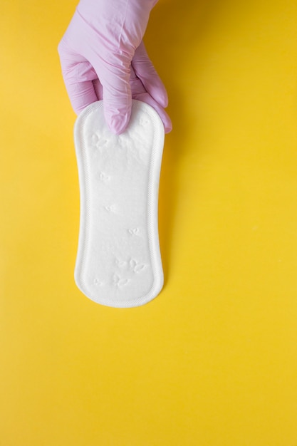 A pink-gloved hand holds a daily thin menstruation pad during the menstrual period of a woman on critical days