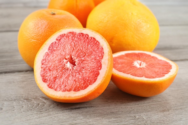 Pink grapefruit cut to half on wood desk, with whole citruses in background.