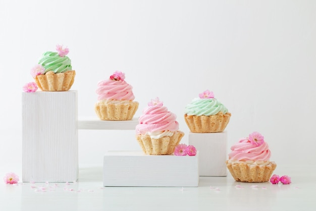 Pink and green cupcakes with spring flowers on wooden podiums on white background