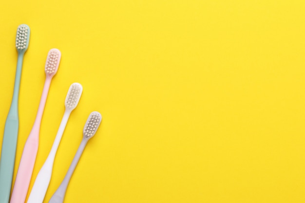 Pink, green, white and gray toothbrushes on yellow wall. 