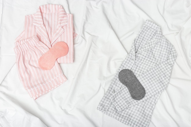 Pink and grey pajamas and eye mask on white sheet on bed. Night suit for sleeping. 