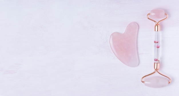 핑크 구 아샤 페이셜 마사지 도구. 핑크 나무 표면에 로즈 쿼츠 옥 롤러. 공간을 복사하십시오.