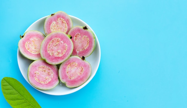 Pink guava in white plate on blue background.