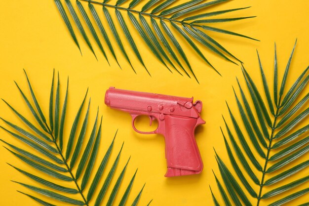 Photo pink gun and palm leaves on yellow background tropical minimal layout top view flat lay