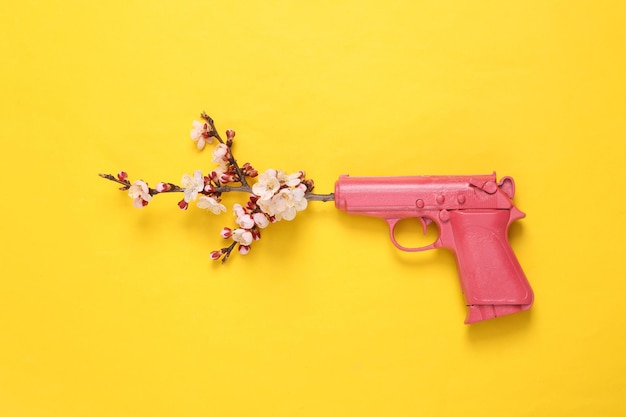 Photo pink gun with beautiful flowering branches on yellow background minimal concept flat lay top view