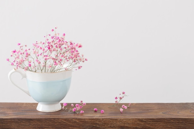 Pink gypsophila in blue cup on  wooden shelf on  white background