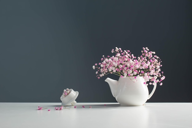 Pink gypsophila in white teapot on background gray wall