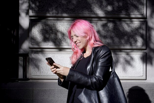 Pink hair woman dressed in black leather writing a message on her cell phone