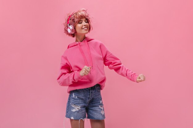 Pink-haired curly woman in headphones dances and listens to music