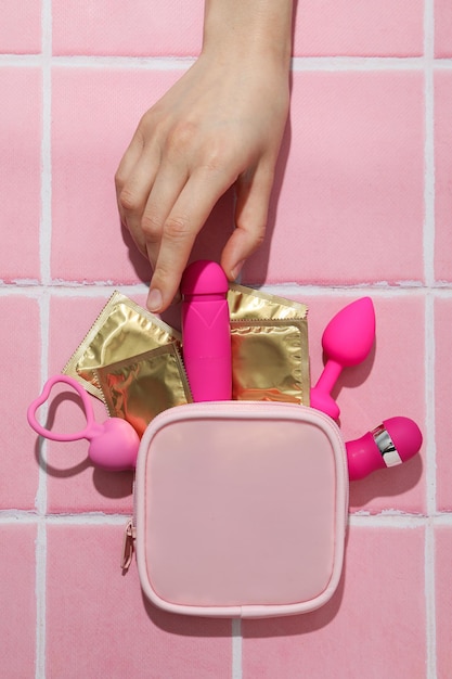 Pink handbag with condoms and sex toys on a pink background