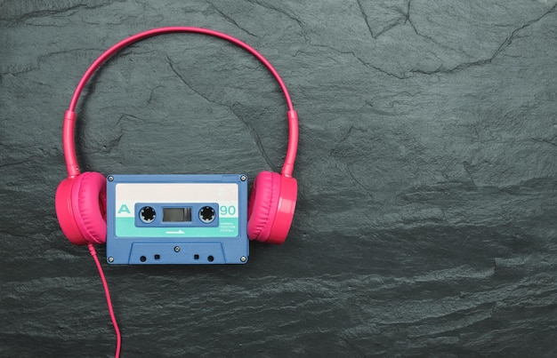 젖은 슬레이트 배경에 있는 분홍색 헤드폰과 파란색 테이프 오디오 카세트
