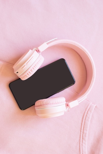 Pink headphones and smartphone on a pink background. Concept for music, podcasts, audiobooks. Top view, copy space.