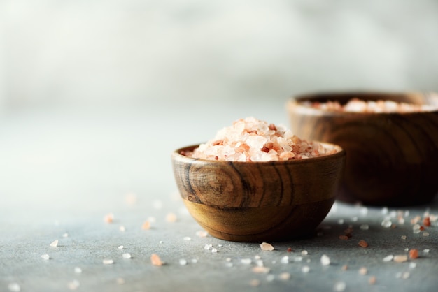 Pink Himalayan salt crystals and powder in wooden bowls on grey concrete. Healthy diet without salt. 