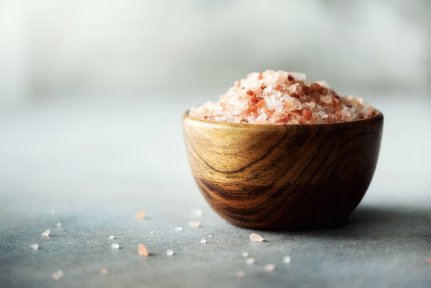 Photo pink himalayan salt crystals and powder in wooden bowls on grey concrete. healthy diet without salt.