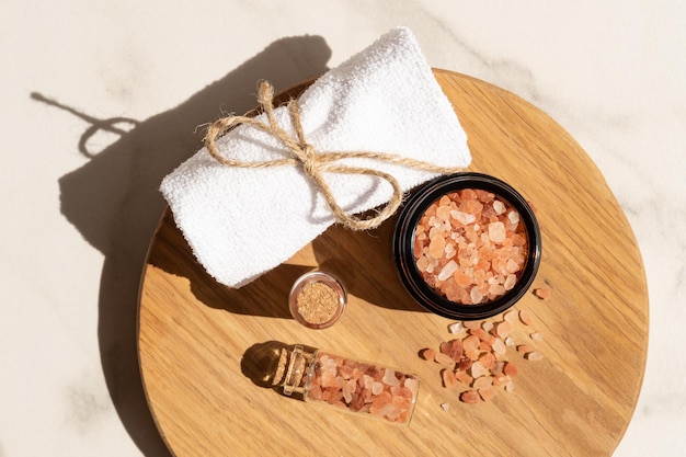 Pink Himalayan salt in the glass bottles with rolled towel on wooden board Close up of pink crystals of sea salt Spa body care concept