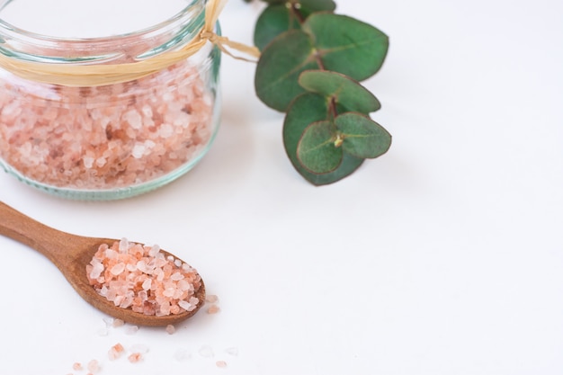 Pink Himalayan salt in glass jar wood spoon eucalyptus branch on white background