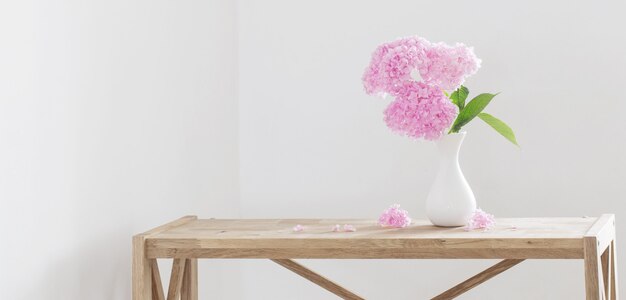 Pink   hydrangea in white vase on wooden shelf  on background white wall