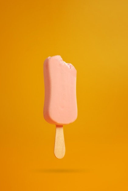 Pink ice cream popsicle on yellow background bitten off a piece hanging in the air