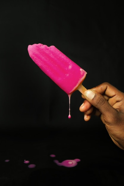 Pink ice cream on a stick in hand on a black background