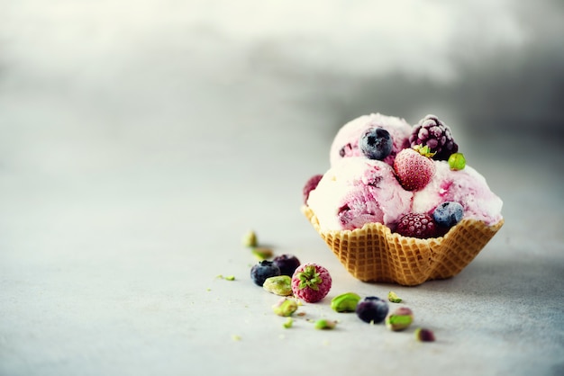 Pink ice cream with berries, strawberries, blueberries, raspberries, pistachios in waffle basket. Summer food concept, copy space. 