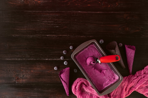 Gelato rosa con una spatola per gelato su un fondo di legno scuro con tazze di cialde