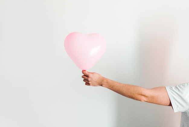 Pink inflatable heartshaped balloon in hand White background