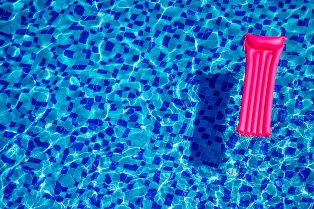 Pink inflatable mattress on blue turquoise water swimming pool copy space top view