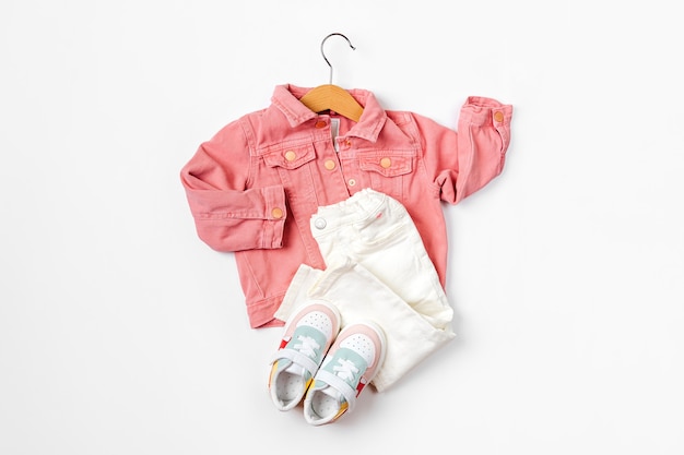 ハンガーにピンクのジャケットとスニーカーのパンツ。白地に春、秋、夏のベビー服とアクセサリーのセットです。ファッションキッズ衣装。フラットレイ、上面図