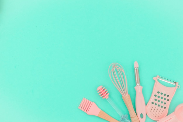 pink kitchen utensils on neo mint background. Greater, whisk and iron cooking form. Top view