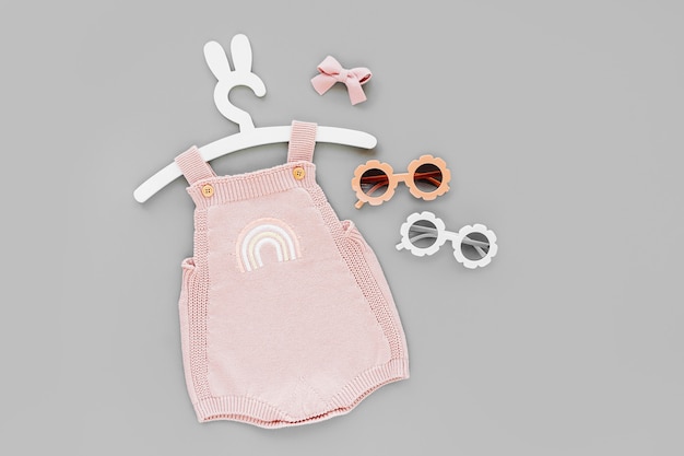 サングラスをかけたバニーの耳が付いたかわいいハンガーのピンクのニットボディスーツ。夏用の子供服とアクセサリー。ファッション新生児。フラットレイ、上面図